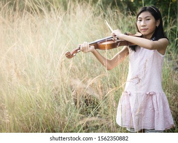 Asian Girl Playing Violin In The Grass With Sun Light.