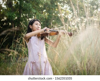 Asian Girl Playing Violin In The Grass With Sun Light.