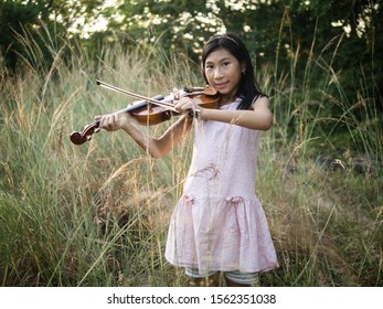 Asian Girl Playing Violin In The Grass With Sun Light.