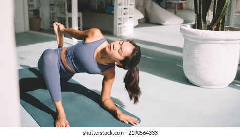 Asian Girl Practicing Yoga On Fitness Mat At Home. Concept Of Healthy Lifestyle. Young Attractive Brunette Woman With Closed Eyes Wearing Sportswear And Barefoot. Spacious Apartment At Sunny Day