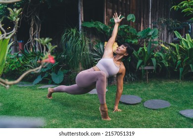 Asian Girl Practicing Yoga In Recolver Side Angle Pose Outdoor. Concept Of Harmony And Mental Health. Young Athletic Woman Wearing Sportswear And Barefoot On Green Grass In Yard On Bali Island