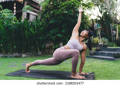 Asian Girl Practicing Yoga In Recolver Side Angle Pose Outdoor. Concept Of Healthy Lifestyle. Young Focused Athletic Woman Wearing Sportswear And Barefoot On Fitness Mat In Yard On Bali Island