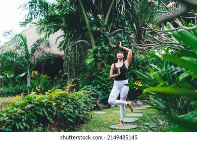 Asian Girl Practicing Yoga In Tree Pose Outdoor. Concept Of Harmony And Mental Health. Young Beautiful Athletic Woman Wearing Sportswear And Barefoot In Tropical Garden. Bali Island. Daytime