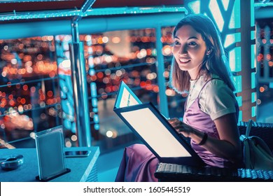 Asian Girl Reads The Menu At The Bar On The Outdoor Roof Terrace Overlooking The Night City