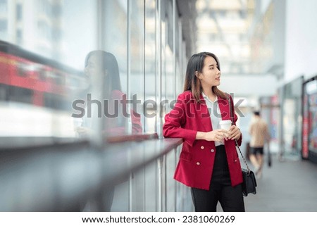 Asian girl relax with a office cup in worker uniform Stand in a department store with glass walls and see a view of the city and train tracks in the glass.