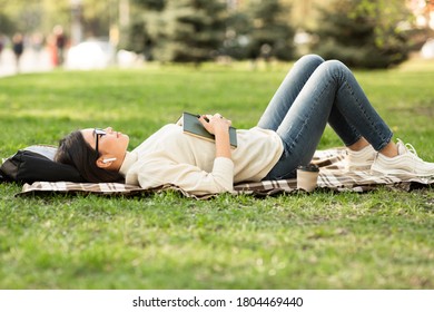 Asian girl relaxing, lying in park, listening to audio podcast, free space