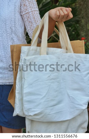 Asian girl show many blank linen nature canvas tote bag with green garden background.Use tote bag for Replacement plastic bag can save the earth.Reduce global warming concept.Vertical line.