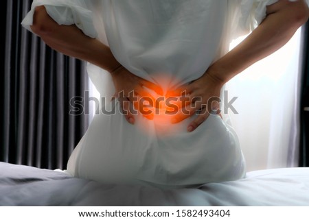 Asian girl sitdown at the bed and hold hand at low backache likes pain this area, may be happen from office syndrome or play sport. She's want to first aid or go to the hospital and meet the doctor