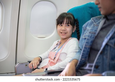 Asian Girl Sitting At Airplane Cabin Seat Talking With Mother During Flight Departure. Airline Travel On Vacation