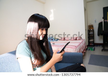 An Asian girl sitting on the couch using a mobile phone. Use mobile video, self-timer, and listen to music.
