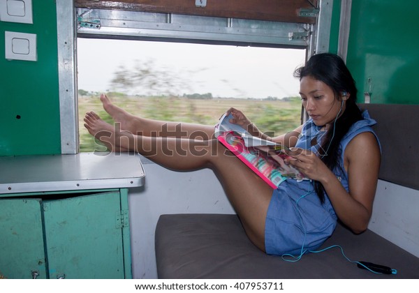 Asian\
girl sitting in a train with her legs on window, Burma. Passenger\
sitting on bed beside the window of a moving train. Entertainment\
in sleeper train compartment of Myanmar\
railways,