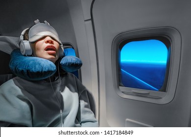 Asian Girl Sleeping In Her Seat On The Plane Near The Window In A Mask And With A Pillow To Sleep. The Concept Of Travel With Comfort And Jetlag