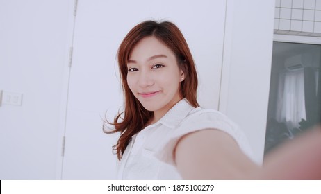 ฺBeautiful Asian Girl Smiling And Show Her Hand In A White Shirt Takes A Video Selfie With A Friend In A White Room.