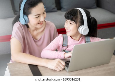 Asian Girl Student With Parent Online Learning Study Online Class Video Call Teacher. Kid And Mom Wearing Headset And Using Laptop At Home