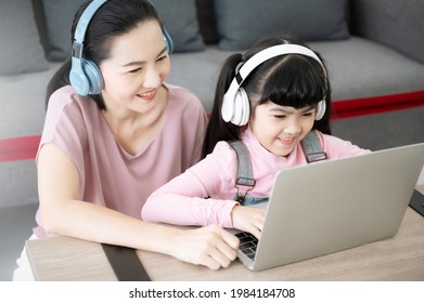 Asian Girl Student With Parent Online Learning Study Online Class Video Call Teacher. Kid And Mom Wearing Headset And Using Laptop At Home