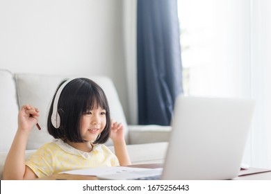 Asian Girl Student Wear Wireless Headphone Study Online With Video Call Teacher, Happy Young Girl Learn English Language Listen Lecture Watch Write Notes Look At Laptop At Home.Covid-19 Coronavirus.