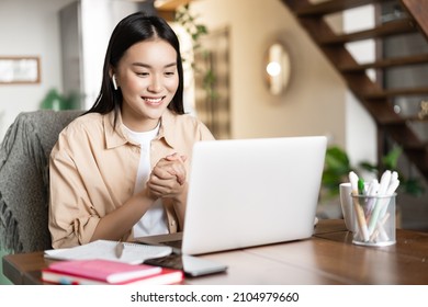 Asian girl studies at home using laptop computer. Young woman attends online classes, webinar or video conference, working on pc from home