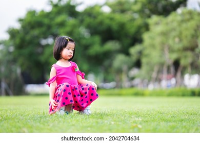 Asian Girl Sulky. Cute Girl Was In A Bad Mood, A Lonely Child Sat Alone On A Soccer Ball In The Middle Of A Green Lawn. 4-5 Year Old Are Dealing With Her Own Emotions.