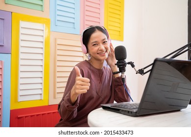 An Asian Girl Talking Into Microphone While Recording Video Blog With Thumbs Up