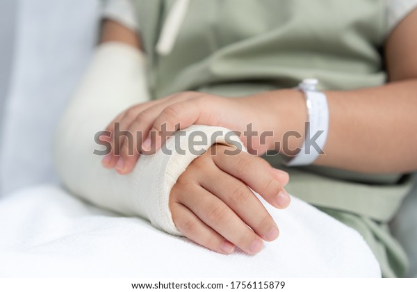Asian girl treatment in hospital lying\
on the bed hurting with broken arm back from\
surgery.