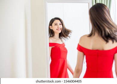 asian girl trying red dress and looking in mirror cheerful 