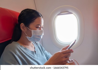 Asian Girl Use A Protection Mask For Coronavirus Or Covid 19 In Airplane. Thai Lady Playing With Her Phone On Airplane.