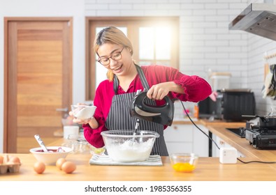 Asian girl using the blender, blend dough and other ingredients for cooking the chocolate cake with happy feeling in the kitchen room. 