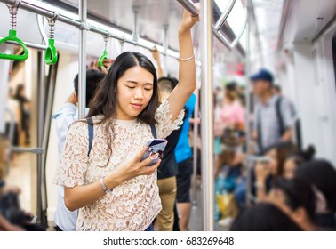 Asian Girl Using Phone On Busy Subway Train