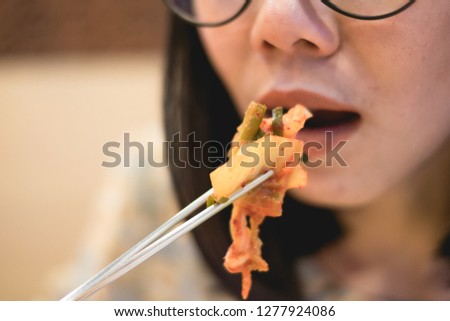 An asian girl is using silver chop stick to feed kimchi in her mouth.