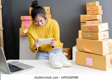 Asian Girl Using Smartphone To Shoot White Sneaker Posted For Sale On The Internet.startup Small Business Owner Working With Tablet At Workplace.happy Owner & Seller Check Product Order To Customer