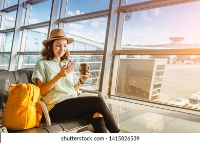 Asian girl waiting for departure at the airport on your vacation. Uses a smartphone and drinks coffee - Shutterstock ID 1415826539