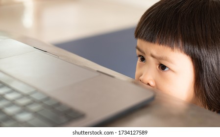 Asian Girl Watching A Scary Cartoon Online From A Notebook Computer, Which Has A Facial Expression And A Bright Expression Of Fear And Concern.