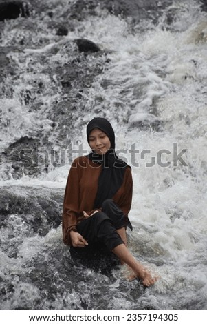 An Asian girl wearing a hijab poses in a river with flowing water.