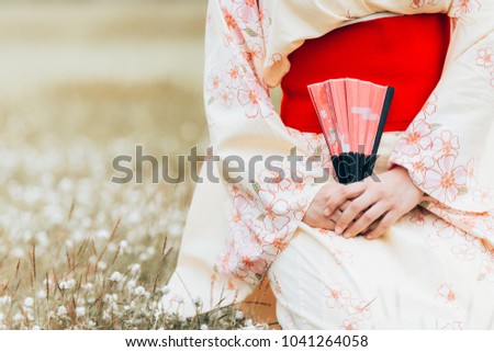Asian girl wearing a kimono sitting holding fan on a green grass
