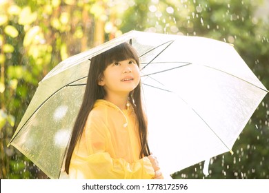 Asian Girl Wearing Yellow Raincoat And Enjoying Rainfall In The Park. Kid Playing On The Nature Outdoors. 