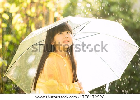 Asian girl wearing yellow raincoat and enjoying rainfall in the park. Kid playing on the nature outdoors. 