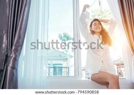 Asian girl who just wake up in the morning as relaxed and smiling. She opened the window to receive the light of the morning sun. 