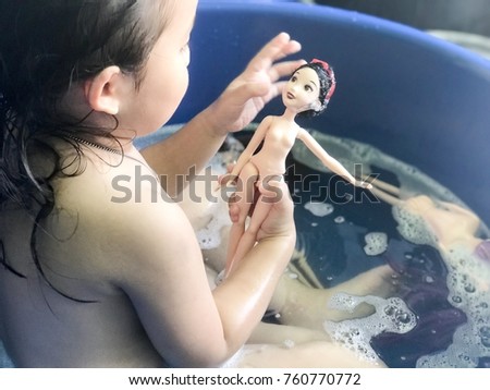 An asian girl who is playing the barbies doll and taking a bath in the bathtub