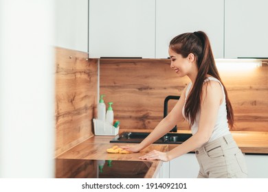 Asian Girl Wipes Wooden Kitchen Countertop In The Afternoon Home. Cleaning. Girl Washes The Kitchen