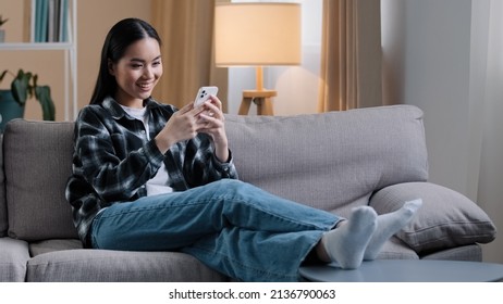 Asian Girl Woman Sitting On Sofa At Home Relaxing Watching News Feed On Social Media Choosing Clothes Online Shop Internet Store Dating Site Wi-fi Smartphone Shopping Post Stories Swipe Touchscreen