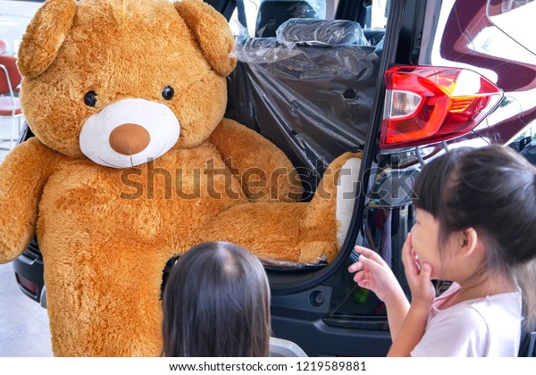 Asian girls laugh\
at a big brown bear doll 