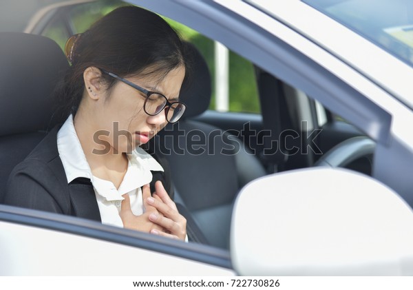 Asian glasses business woman having\
chest pain from heart attack while driving a car.  Illness,\
exhausted, disease, tired for overtime working\
concept.