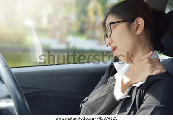 Asian glasses business woman\
having pain on her shoulder, back and neck while driving a car.\
Illness, exhausted, disease, tired for overtime working\
concept.