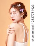 Asian graceful woman poses with delicate butterfly hair accessories perfect clean fresh skin peach-toned background, Female model posing in studio. Face care, Facial treatment, Cosmetology.