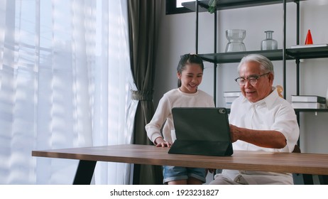 Ein asiatischer Großvater und Enkelin verbringen Zeit zusammen im Wohnzimmer. Fröhlicher Senior Mann mit kleinen Mädchen mit einem Tablet auf dem Tisch zu Hause.