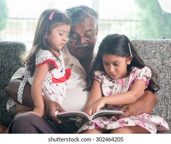 Asian Grandfather And Granddaughters Reading Story Book. Happy Indian Family At Home. Grandparent And Grandchildren Indoor Lifestyle.