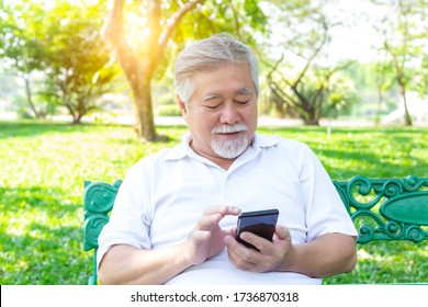 Asian Grandfather Texting To Family By Using Mobile Phone, Internet Online At Park. Old Man Doing On Application Of Net Banking By Transfer Money Elderly Man Get Happy, Convenient When Use Application