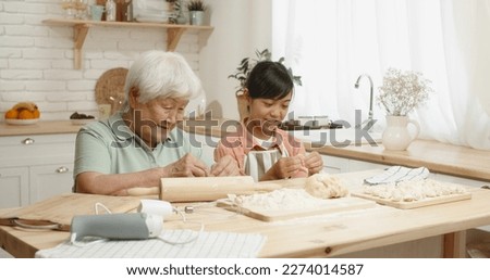 Asian grandmother cooking together with her teen granddaughter, preparing dough for dumplings, spending time together - family ties, concept 