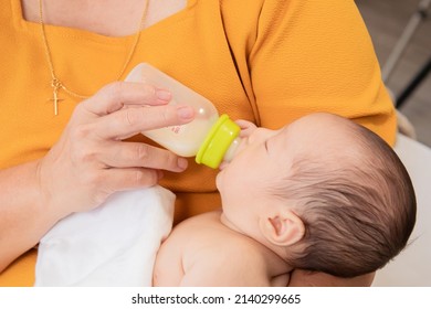 Asian Grandmother Feeding Newborn Baby In Bedroom. Senior Women Taking Care Adorable Infant At Home. Mother Enjoying Feeding Toddler And Feeling Proud. Little Child Hungry In Morning.