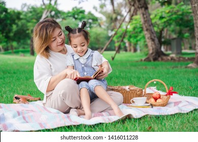 Asian grandmother and granddaughter sitting on the green glass field outdoor, Asian family enjoying picnic together in summer day
